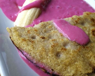 Ein knuspriger Pfannkuchen auf Himbeerjoghurt neben einer Banane mit Mandelversteck